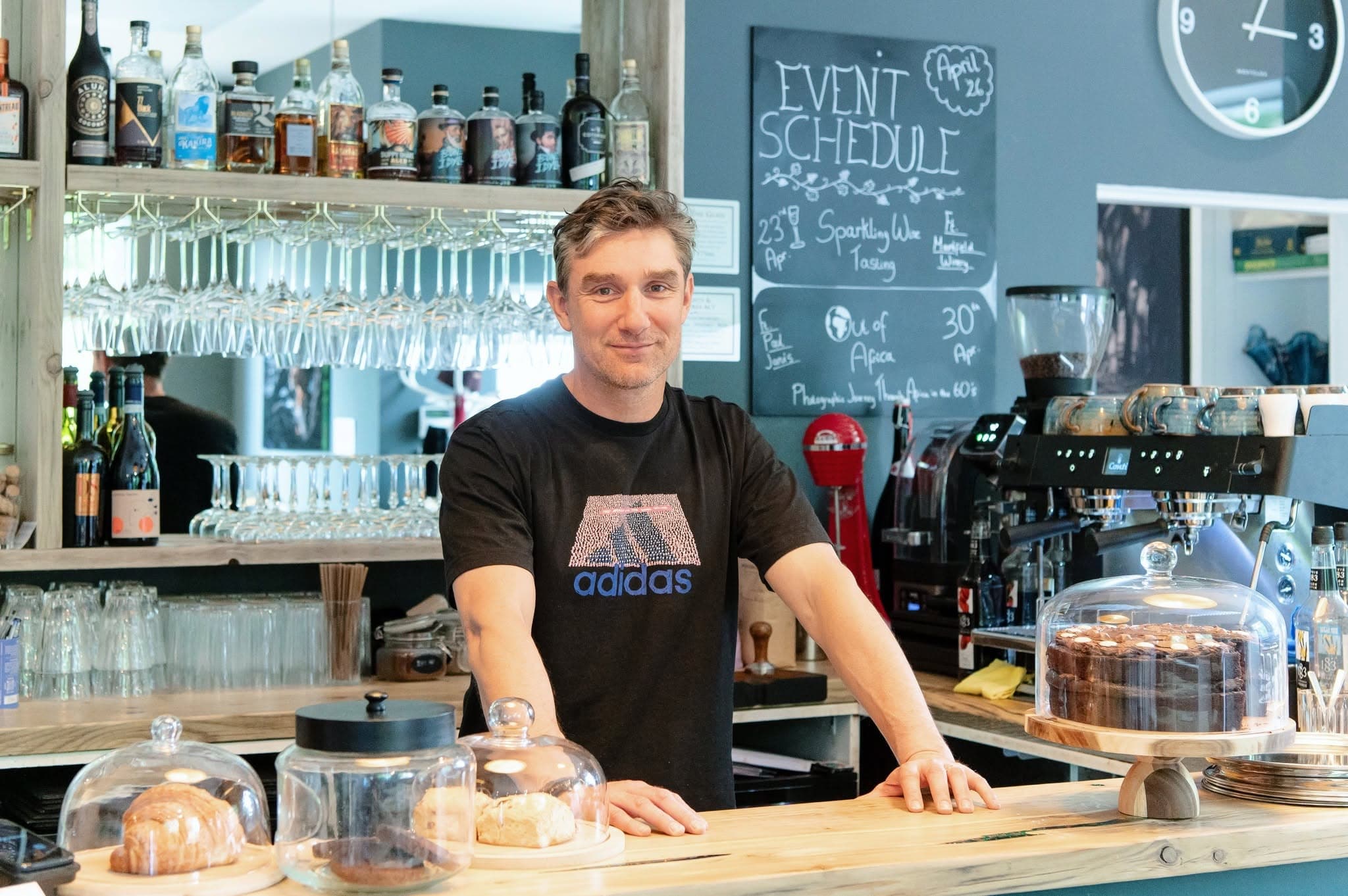 A member of the Blended team behind the bar with fresh pastries and cakes under glass domes
