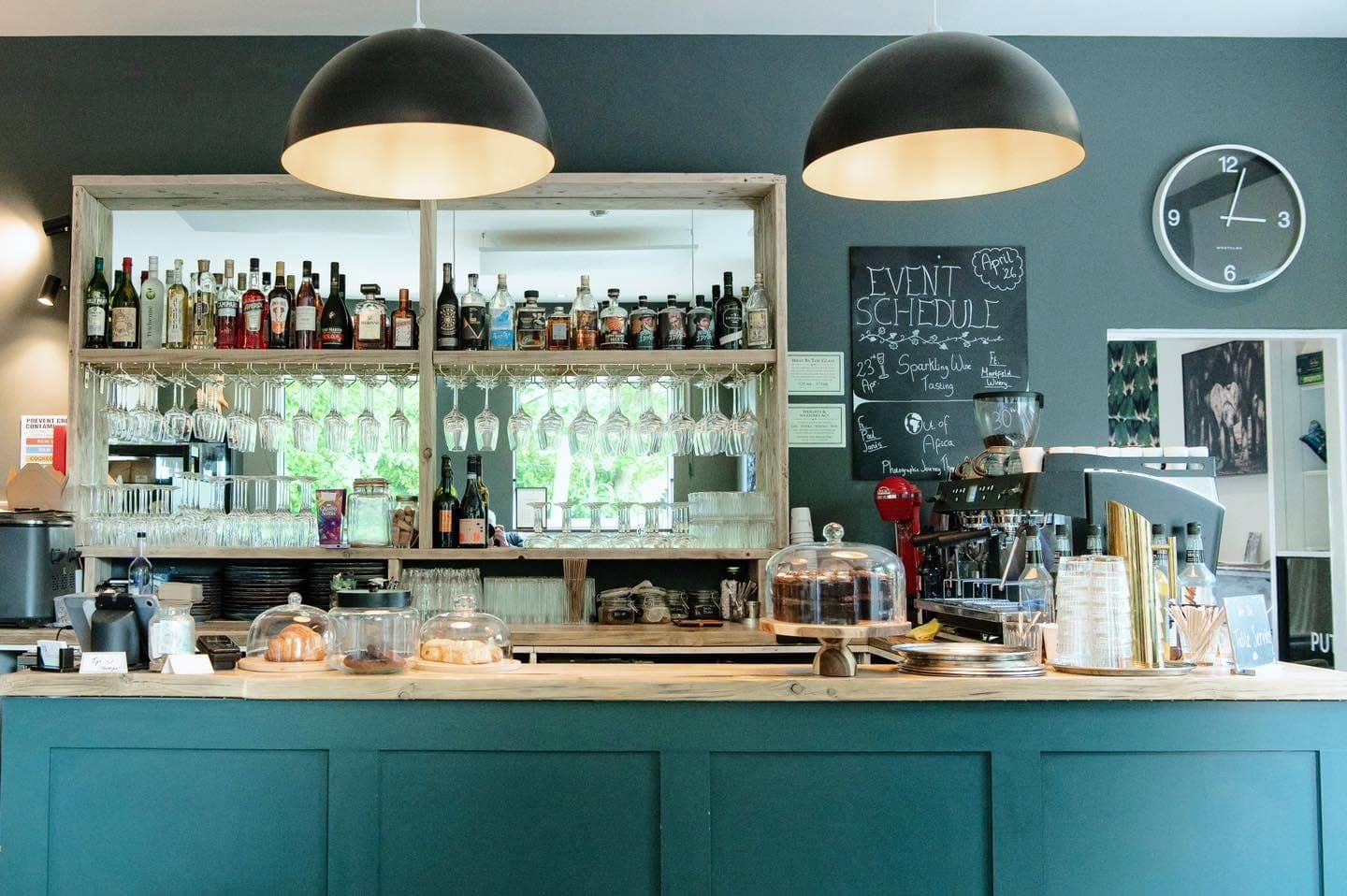 Blended's bar with hanging wine glasses, a spirits shelf and cake stands under dome pendant lights