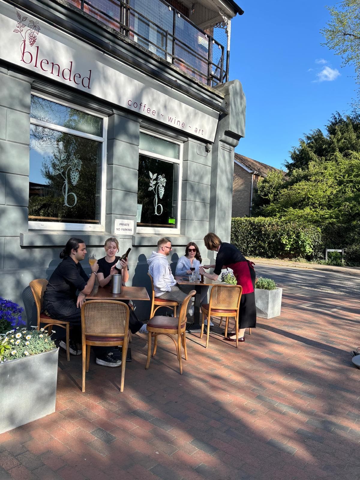 Friends gathered around an outdoor table beside the Blended sign in the sunshine
