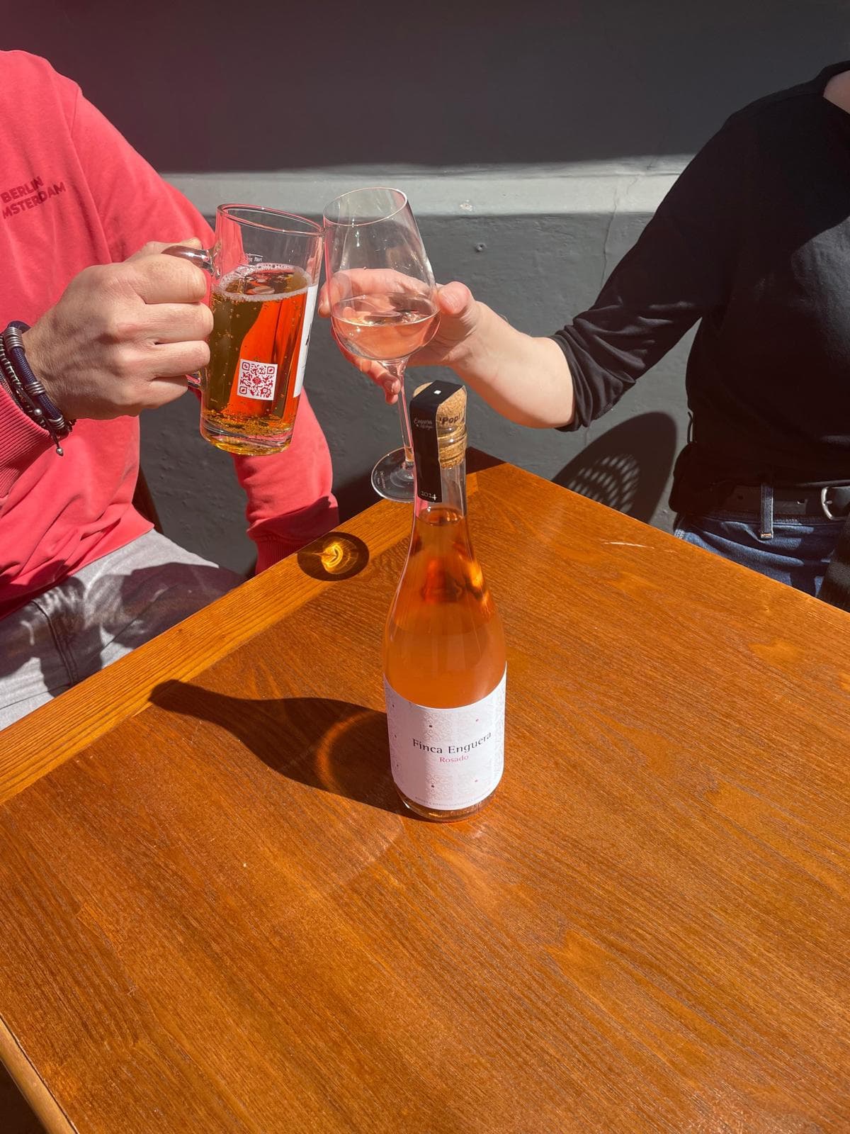 A beer and a glass of rosé clinked together in a toast over a sunlit table